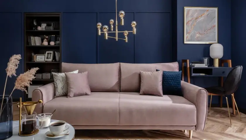 Elegancki salon w stylu art deco z różową sofą, złotym żyrandolem i granatową ścianą.