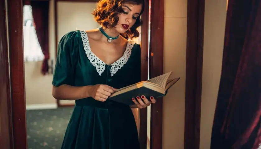 Elegancka kobieta w sukni z lat 40. XX wieku, z koronkowym kołnierzykiem, czyta książkę.