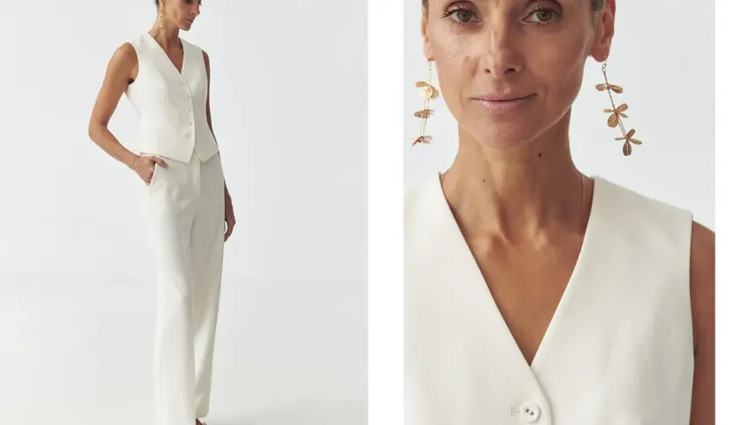 Elegancka kobieta prezentuje, jak nosić kamizelkę damską w stylizacji z białymi spodniami. Długie kolczyki dodają szyku.