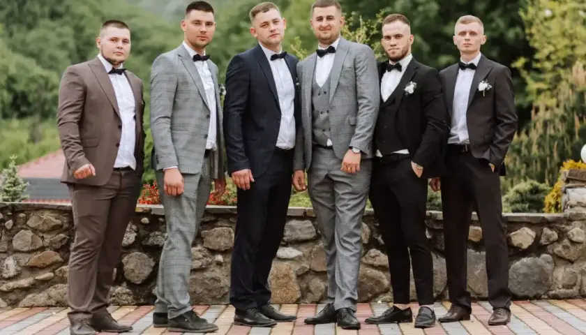 Sześciu mężczyzn w eleganckich garniturach, idealnych na wesele. Różne odcienie szarości, granatu i brązu, każdy z panów prezentuje się stylowo.