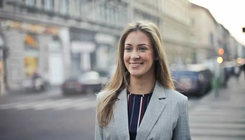 Uśmiechnięta kobieta w marynarce na tle miasta. Jej pozytywne renee opinie o życiu są widoczne w promiennej twarzy.