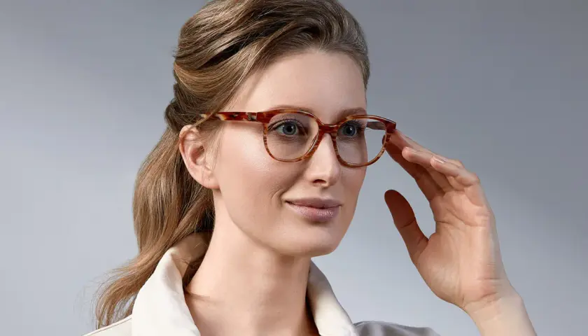 Elegancka kobieta z upiętymi włosami, prezentująca stylowe fryzury do okularów damskie. Jej spojrzenie podkreślają modne oprawki.