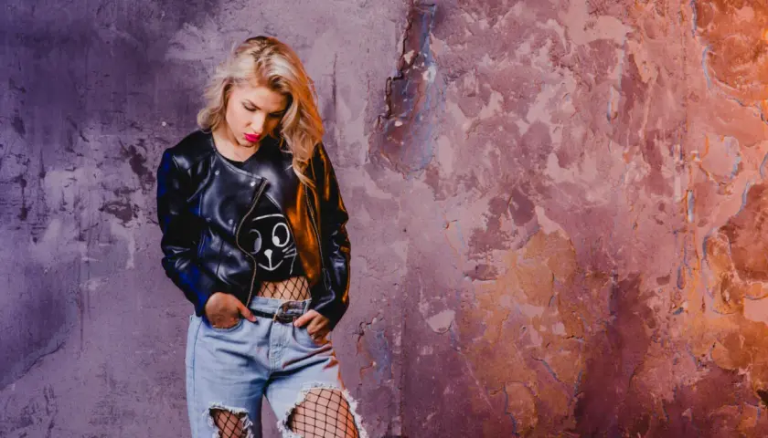 Blondynka w skórzanej kurtce i podartych dżinsach, z siatką na nogach, emanuje grunge'owym klimatem.