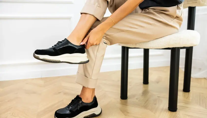 Kobieta poprawia czarne sneakersy na nogach. Dowiedz się, jak szybko wysuszyć buty, by znów cieszyć się komfortem.