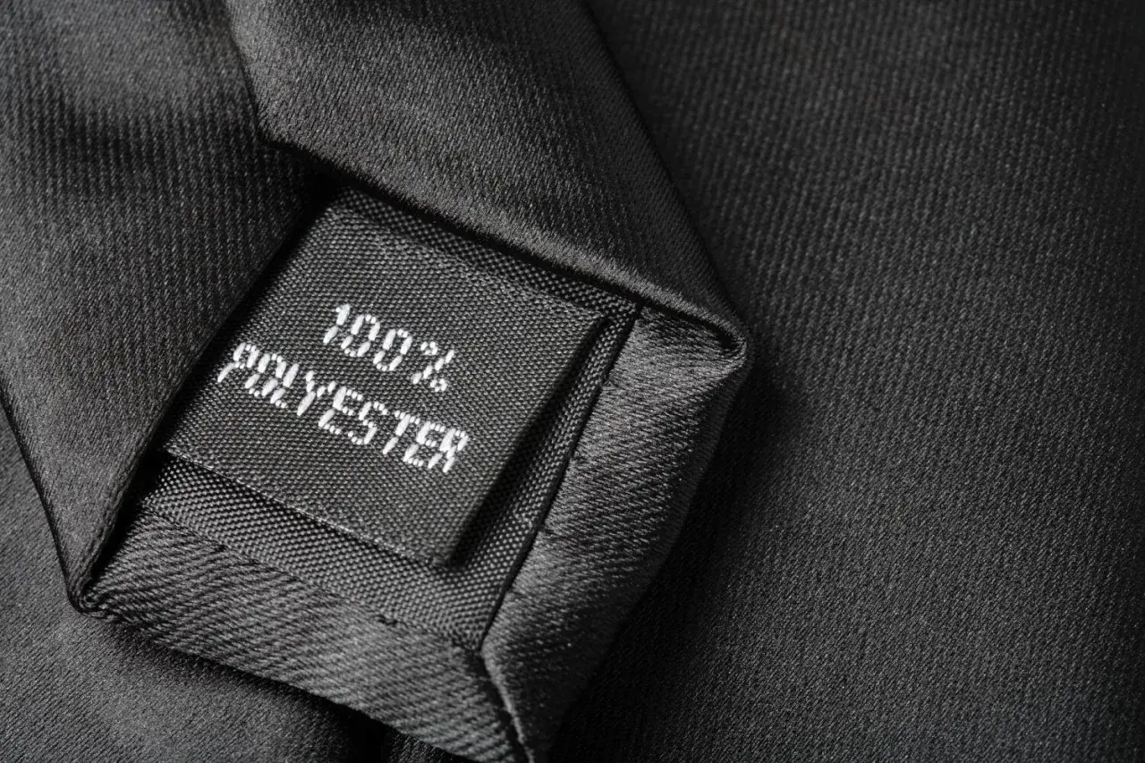 Czarna metka z napisem "100% POLYESTER" na tle eleganckiego materiału. Czy poliester jest zdrowy? To pytanie nurtuje wielu konsumentów.