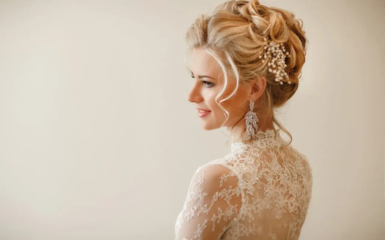 Elegancka fryzura wieczorowa blondynki z perłową ozdobą i długimi kolczykami.