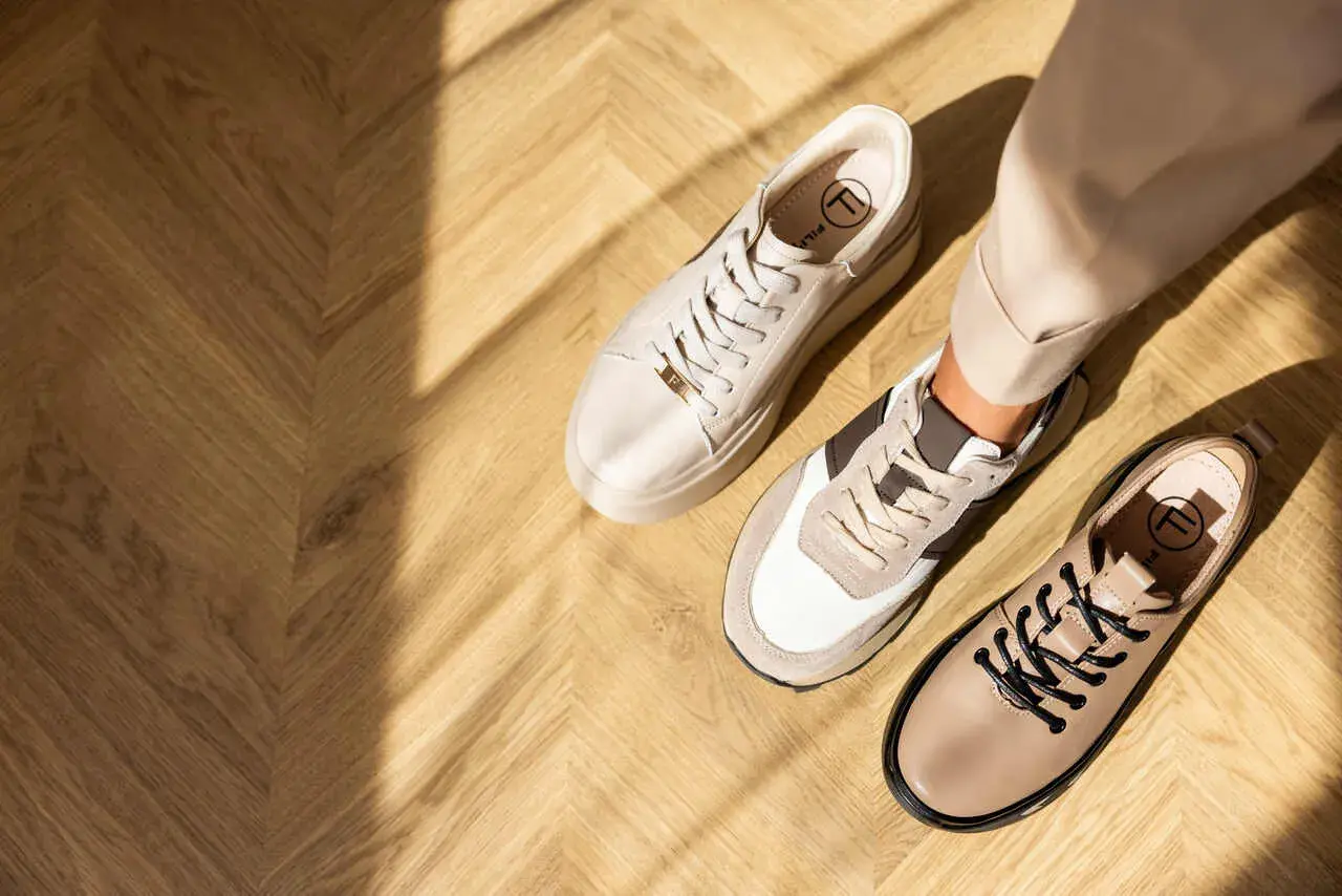 Beżowe sneakersy i półbuty na drewnianej podłodze. Idealne buty do cygaretek dla stylowej kobiety.