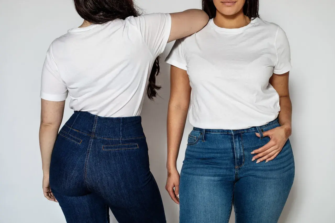 Dwie kobiety w białych T-shirtach i jeansach. Stylizacje z wysokim stanem podkreślają sylwetkę, pokazując jak ukryć brzuch.