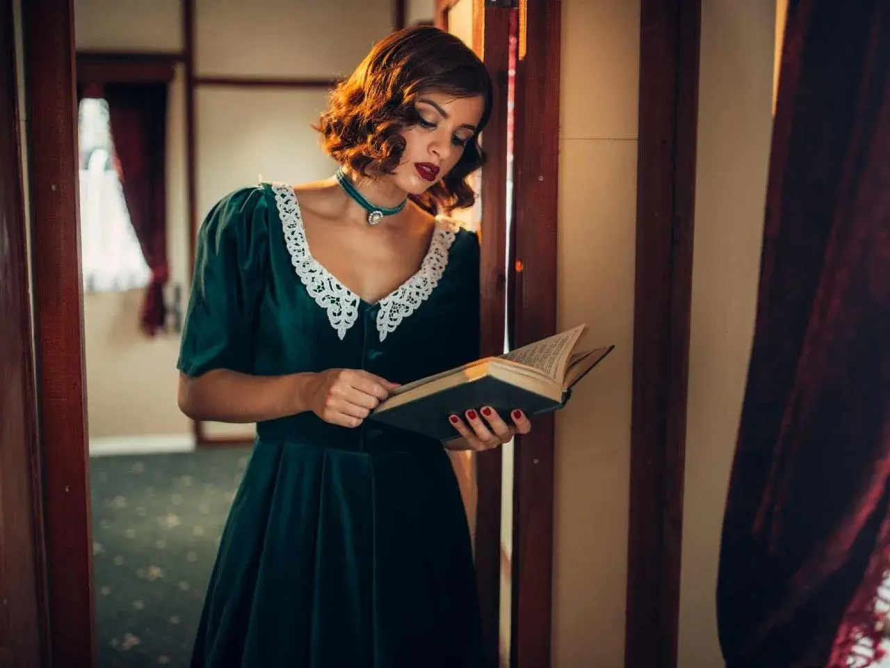 Elegancka kobieta w sukni z lat 40. XX wieku, z koronkowym kołnierzykiem, czyta książkę.