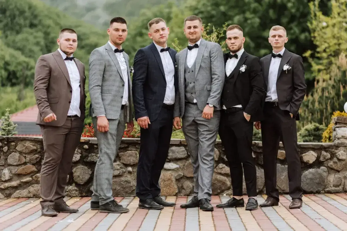 Sześciu mężczyzn w eleganckich garniturach, idealnych na wesele. Różne odcienie szarości, granatu i brązu, każdy z panów prezentuje się stylowo.