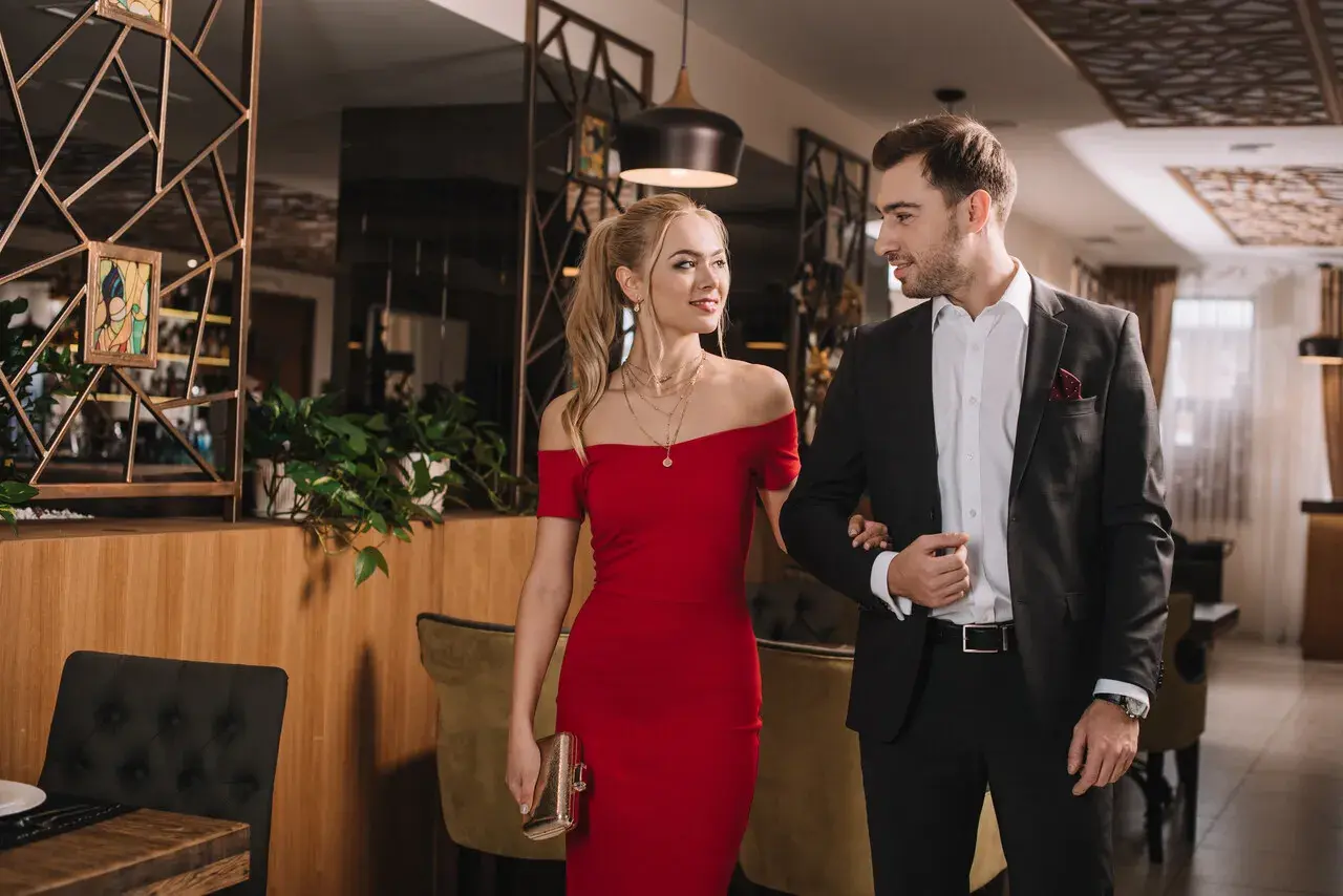Para elegancko ubrana para, ona w czerwonej sukni, on w garniturze, idzie na wieczorne wyjście w stylu cocktail attire.