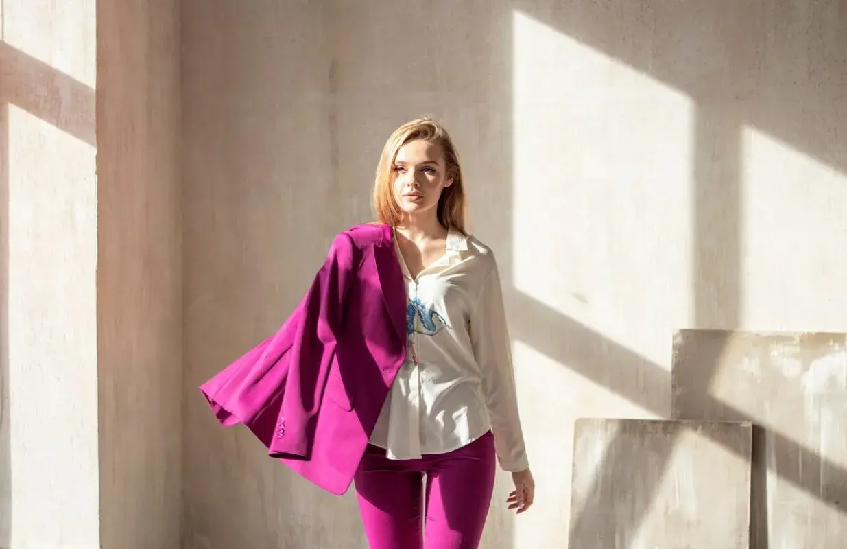 Młoda kobieta w eleganckim garniturze w intensywnym, **magenta kolorze**. Marynarka narzucona na ramię, spodnie podkreślają sylwetkę.