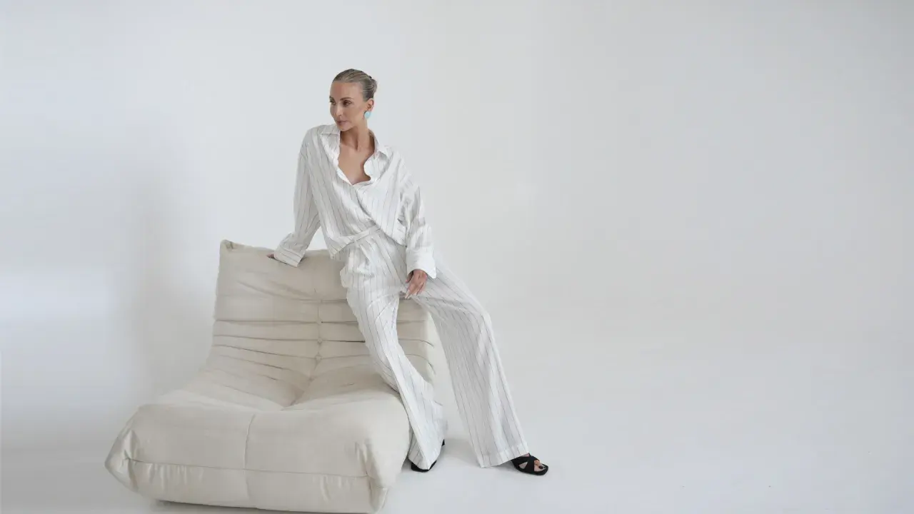 Kobieta w eleganckim, pasiastym komplecie, uosobienie quiet luxury, siedzi na kremowej sofie.