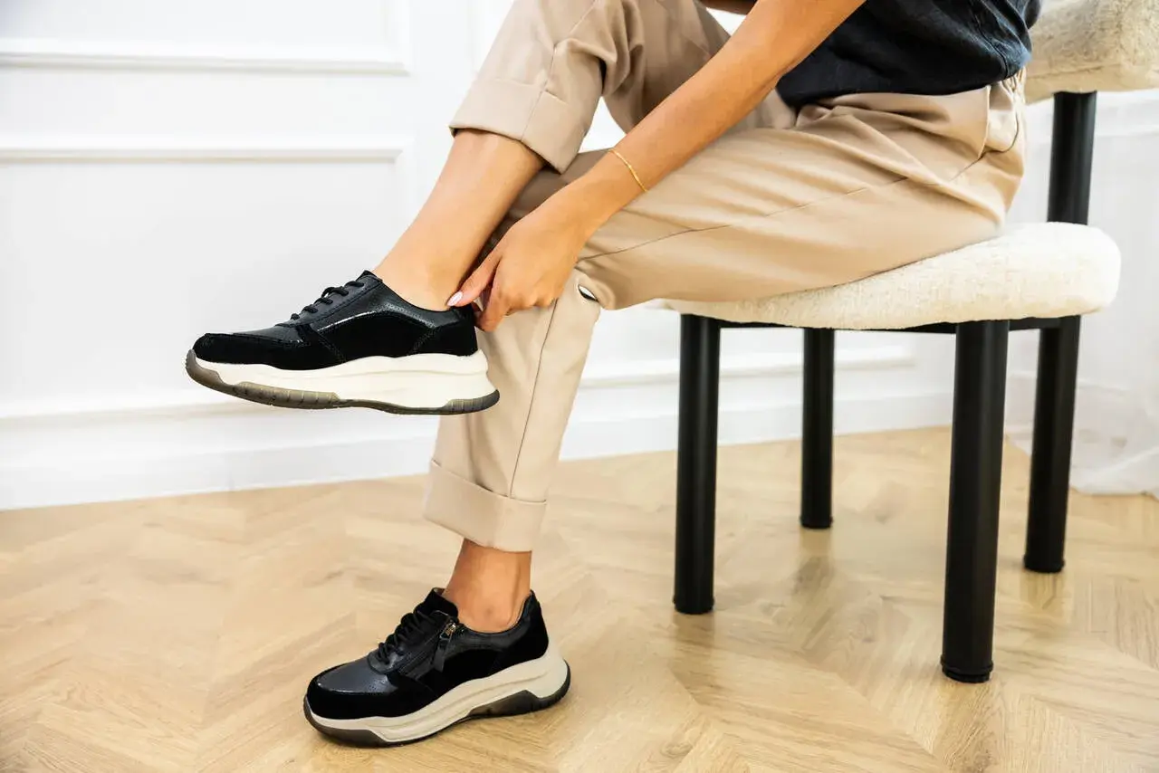 Kobieta poprawia czarne sneakersy na nogach. Dowiedz się, jak szybko wysuszyć buty, by znów cieszyć się komfortem.