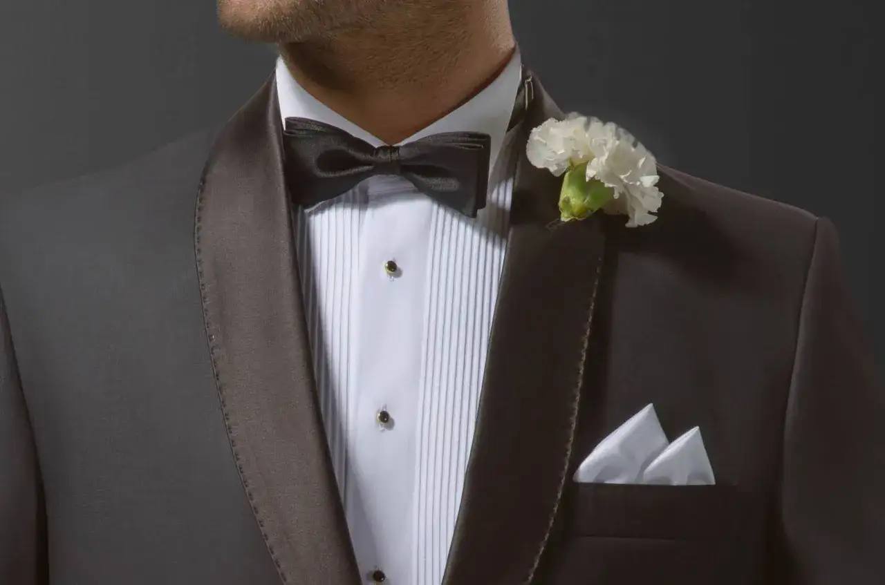 Elegancka stylizacja z czarną muszką i białą butonierką co to jest, ozdobioną kwiatem.