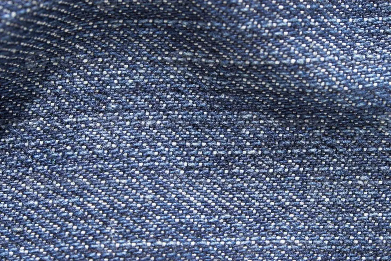 Zbliżenie na niebieski materiał, który jest synonimem słowa denim. Widoczna charakterystyczna, skośna struktura splotu.