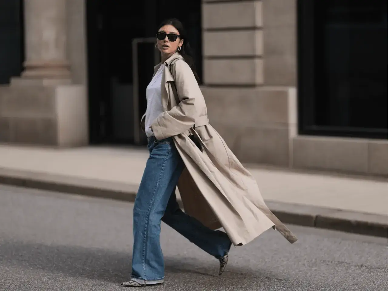 Kobieta w beżowym prochowcu i jeansach, z okularami przeciwsłonecznymi, emanuje stylem clean girl aesthetic.