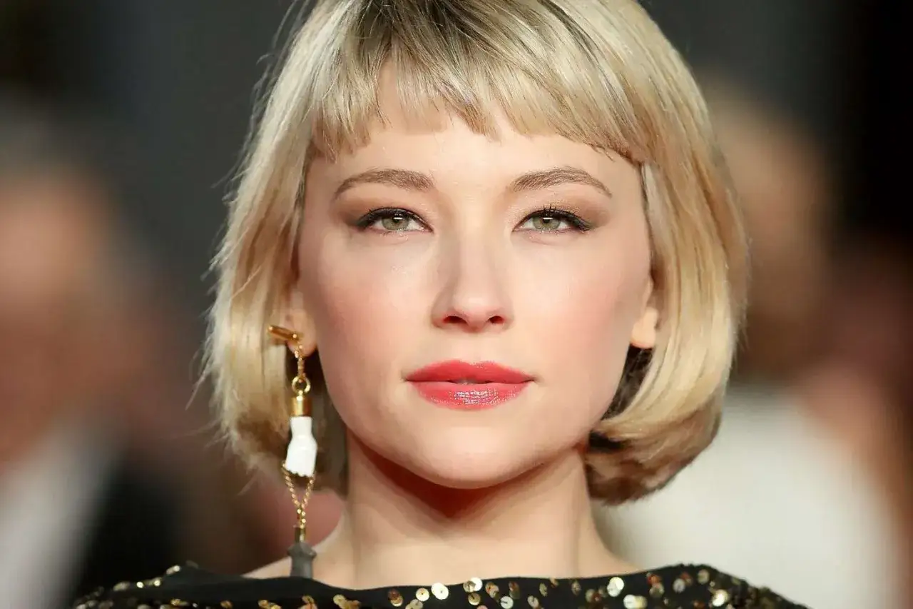 Kobieta z blond krotkimi wlosami z grzywka, zielonymi oczami i wyrazistymi ustami.