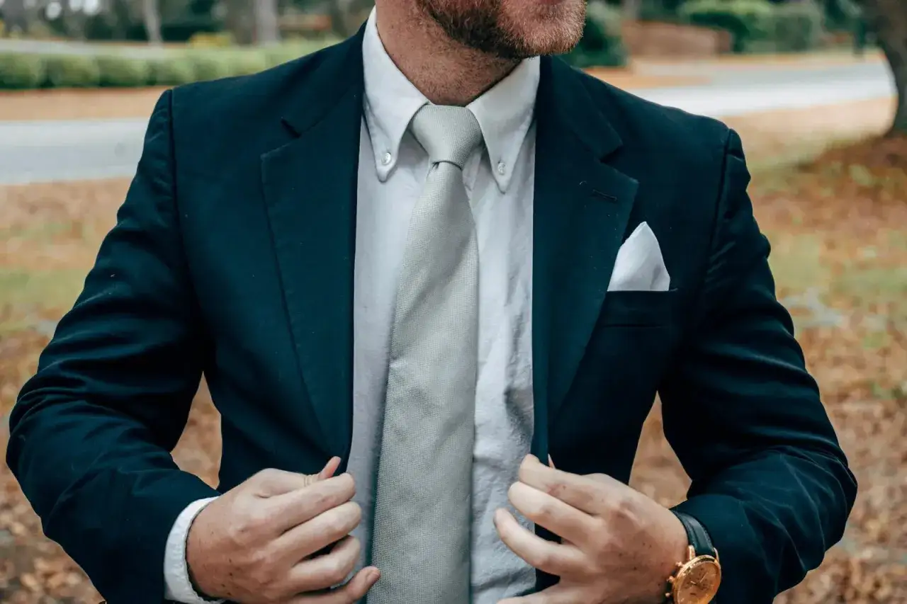 Mężczyzna w garniturze poprawia marynarkę, prezentując idealne wiązanie krawatu. Elegancki styl.