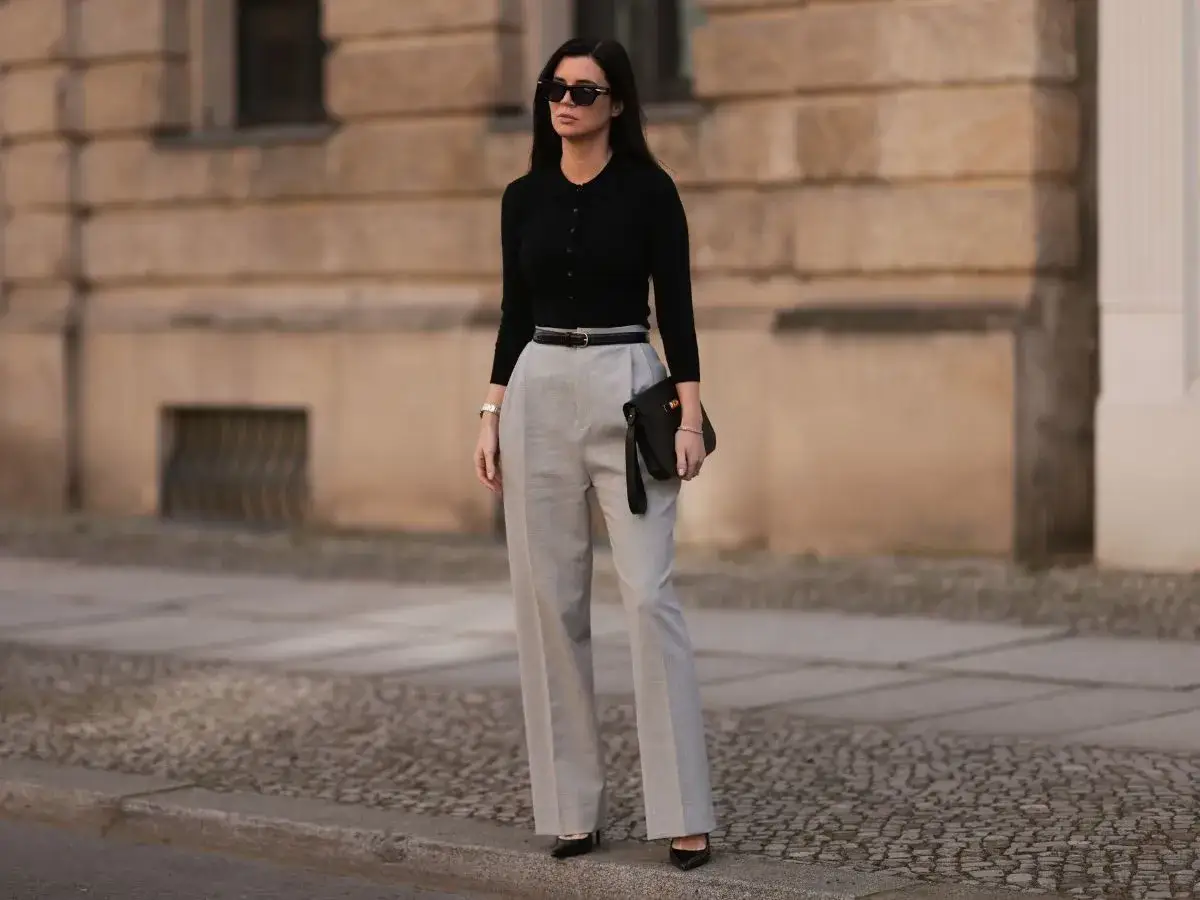 Elegancka stylizacja na imprezę dla 40-latki: czarny dopasowany golf, szare szerokie spodnie, czarna kopertówka i okulary przeciwsłoneczne.