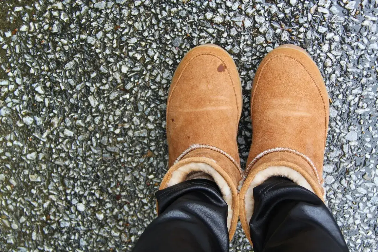 Brązowe zamszowe buty z futerkiem, lekko przybrudzone, stojące na mokrym, kamienistym podłożu. Jak wyczyścić zamszowe buty?
