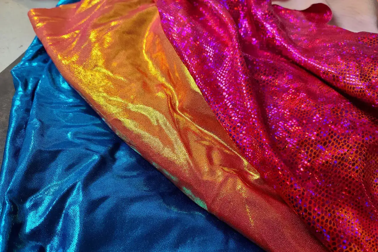 Błyszczące, elastyczne tkaniny w kolorach niebieskim, pomarańczowym i różowym. Spandex to materiał, który nadaje im ten połysk i rozciągliwość.
